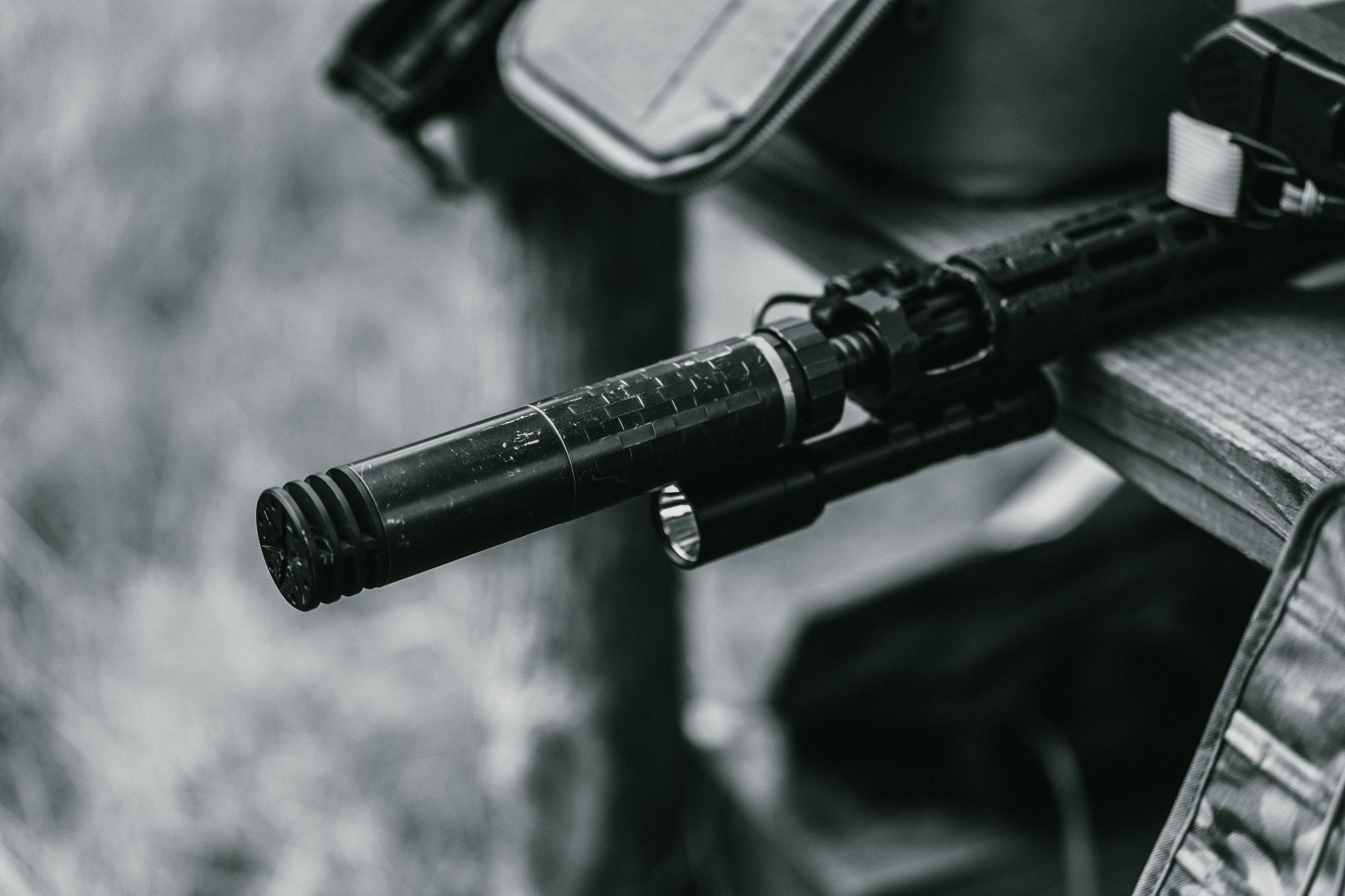 Black and white close-up of a suppressor mounted on a rifle barrel