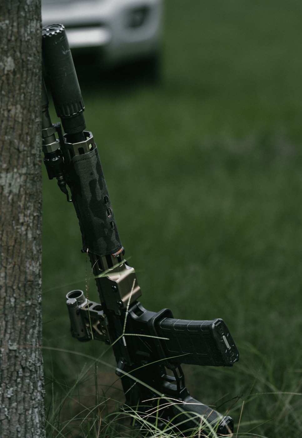 Suppressed rifle resting against a tree