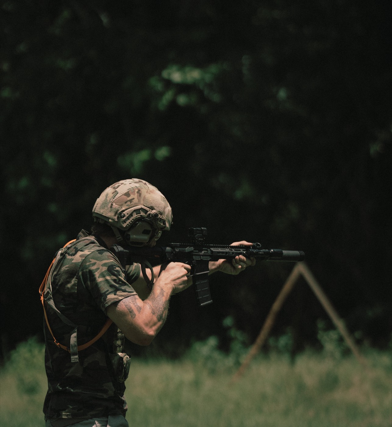 Shooter firing a suppressed AR-15 against a dark treeline